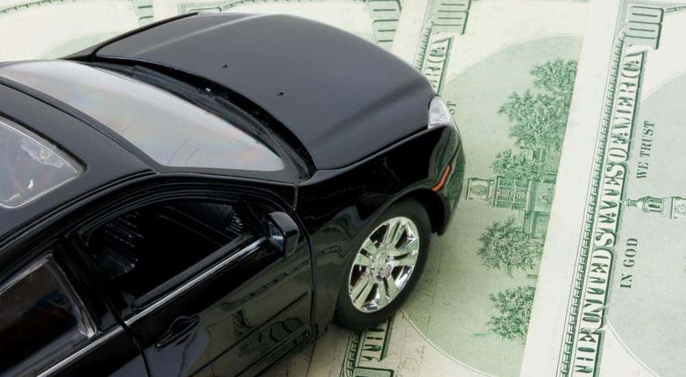 Black toy car on top of one-hundred dollar bills