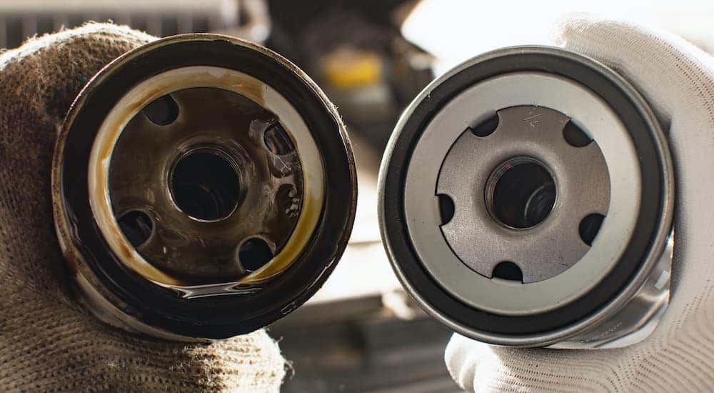 Hands are holding a new and used oil filter side-by-side.