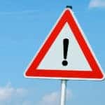 Orange and white triangular sign with a black exclamation point in the center against a blue sky
