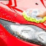 Hand washing a red car with a soapy green cloth