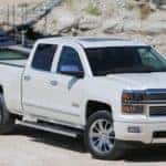 White 2015 Chevrolet Silverado pickup truck parked in front of water and a docked boat