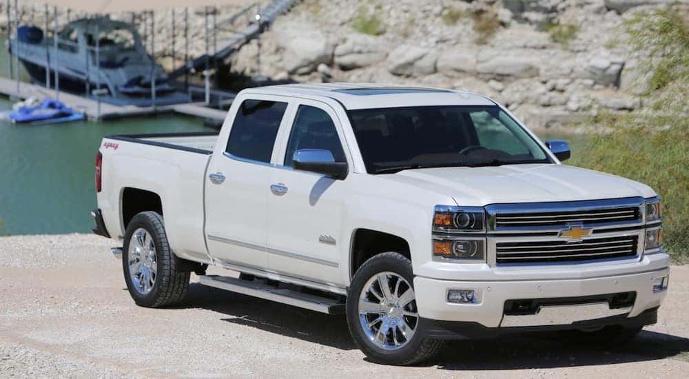 White 2015 Chevrolet Silverado pickup truck parked in front of water and a docked boat