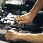 Hands working with tools under the open hood of a vehicle