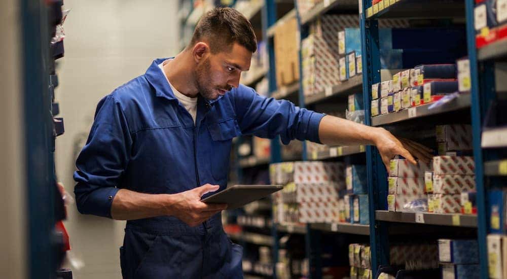 A man in a blue jump suit is shown looking for car parts on a shelf.