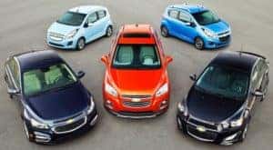 Five Chevy cars from 2014 are parked in an open area at an Albany used car dealership.