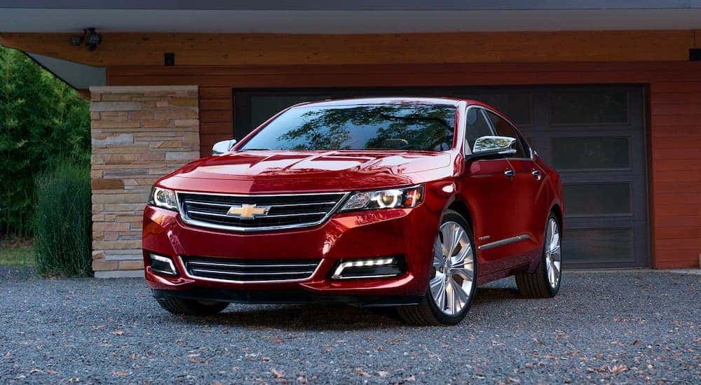 A red 2020 Chevy Impala is parked in front of a garage.