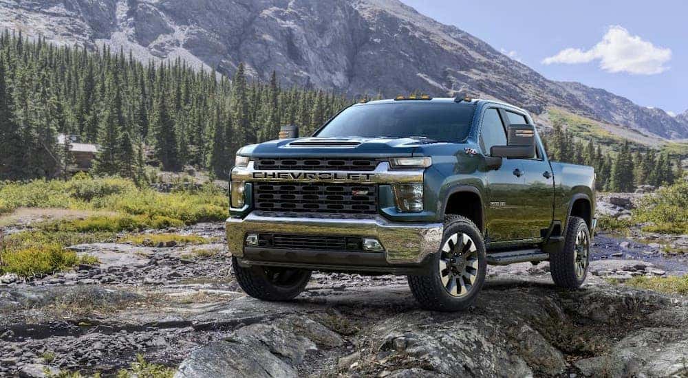 A gray blue 2021 Chevy Silverado 2500HD is parked in front of a mountain and trees.