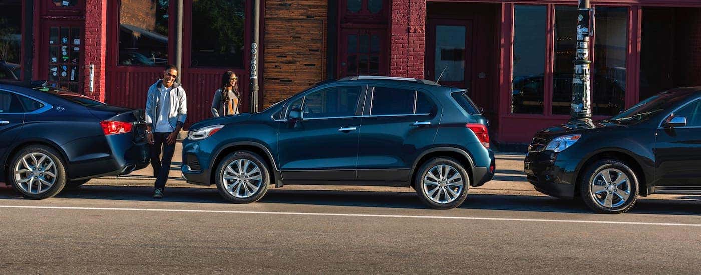 A couple is walking towards a blue 2021 Chevy Trax parked on a street after leaving an Albany car dealership.