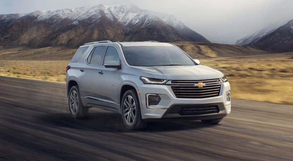 A white 2022 Chevy Traverse is driving on a highway away from snow-covered mountains.