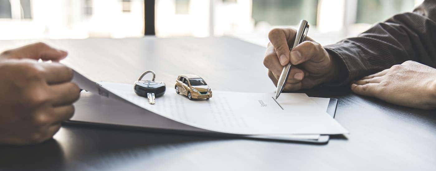 A person is shown signing car financing paperwork at an Albany car dealership.