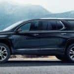 A blue 2021 Chevy Traverse is parked on the pavement with snow covered mountains in the background.