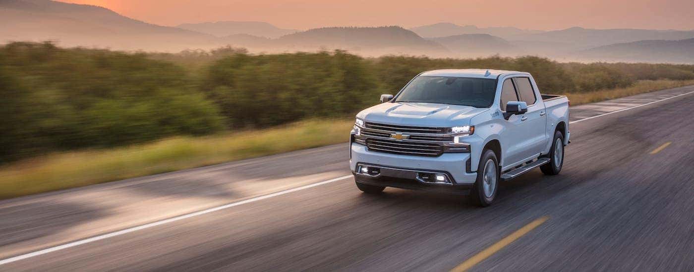 A white 2021 Chevy Silverado is driving on an empty highway at dusk.