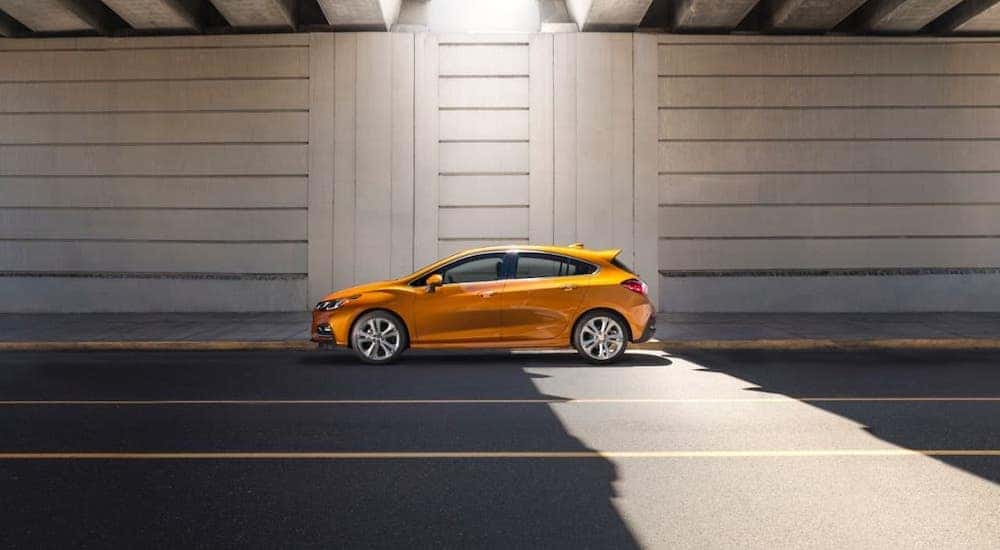 An orange 2017 Chevy Cruze Hatchback is shown from the side driving under a bridge.
