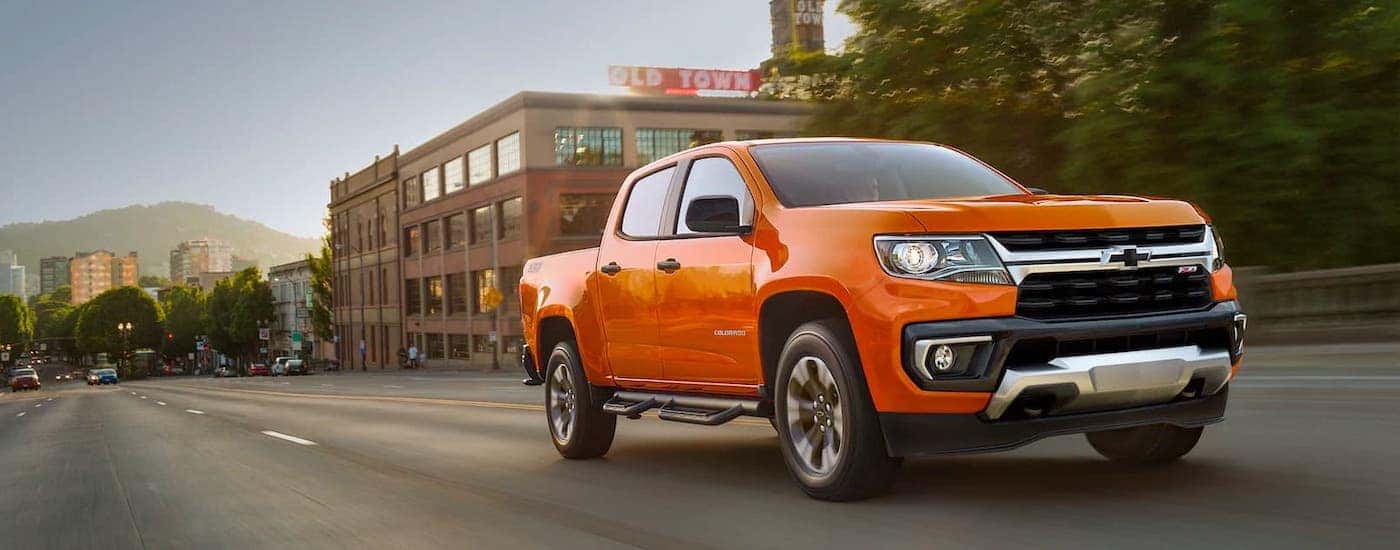 An orange 2021 Chevy Colorado is driving on a downtown street.