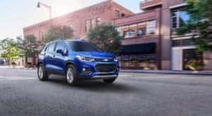 A blue 2021 Chevy Trax from a Capital City Chevy dealership is driving on a city street.