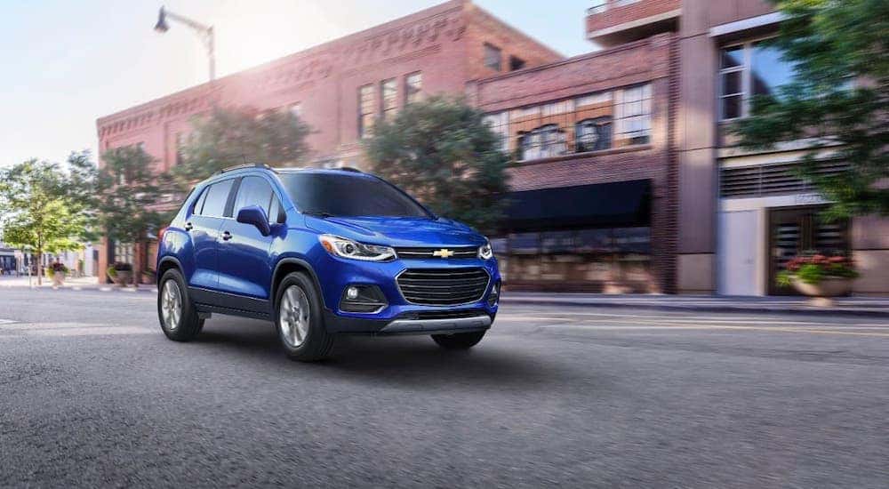 A blue 2021 Chevy Trax from a Capital City Chevy dealership is driving on a city street.