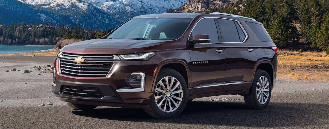 A burgundy 2022 Chevy Traverse is parked in front of a lake and mountains.