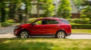 A red 2020 Chevy Equinox is shown from the side driving on a suburban street after leaving a certified pre-owned Chevrolet dealer.