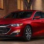 A red 2021 Chevy Malibu is shown parked on the street in front of a brick building.