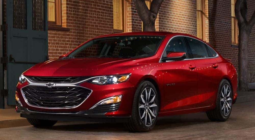 A red 2021 Chevy Malibu is shown parked on the street in front of a brick building.