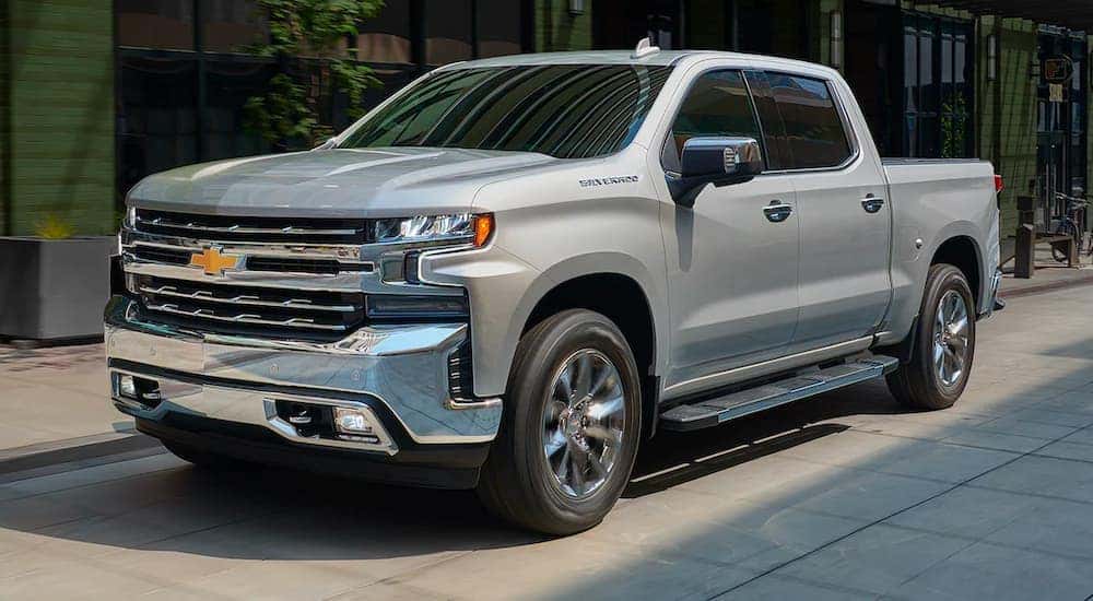 A silver 2021 Chevy Silverado 1500 is shown driving past a row of shops.