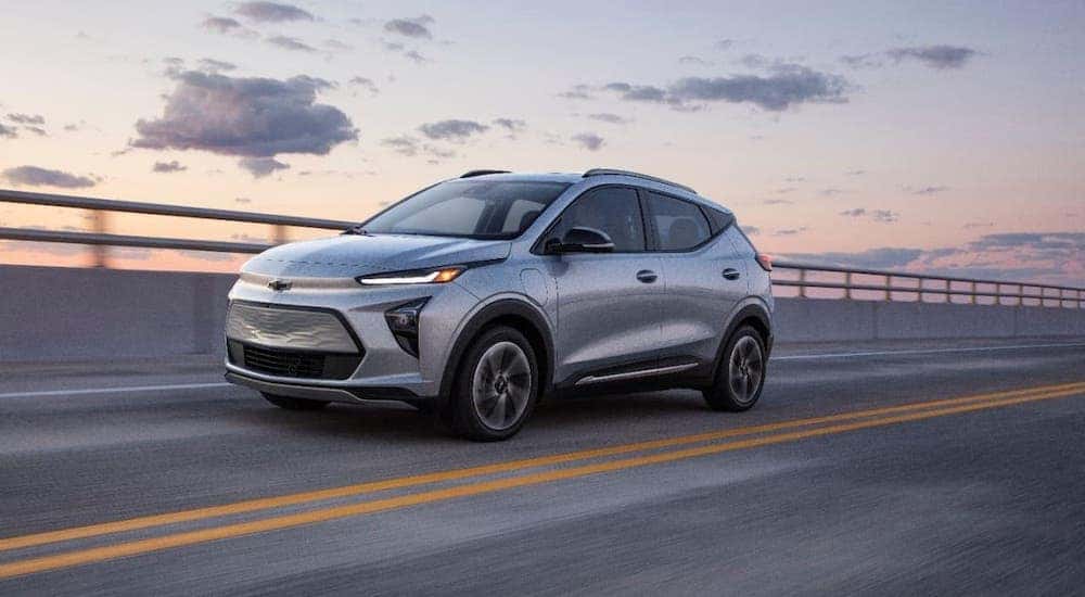 A silver 2022 Chevy Bolt EUV is driving on a highway at sunset after leaving a Chevy dealer near Troy.