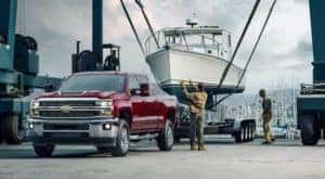 A red 2017 Chevy certified pre-owned Silverado 3500HD is shown parked at a ship yard with a boat being loaded on a trailer.