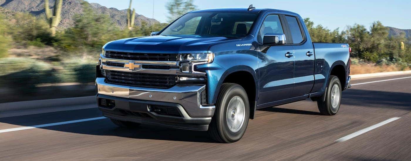 A blue 2019 Chevy certified pre-owned Silverado 1500 Turbo is shown from the side driving down an empty road.