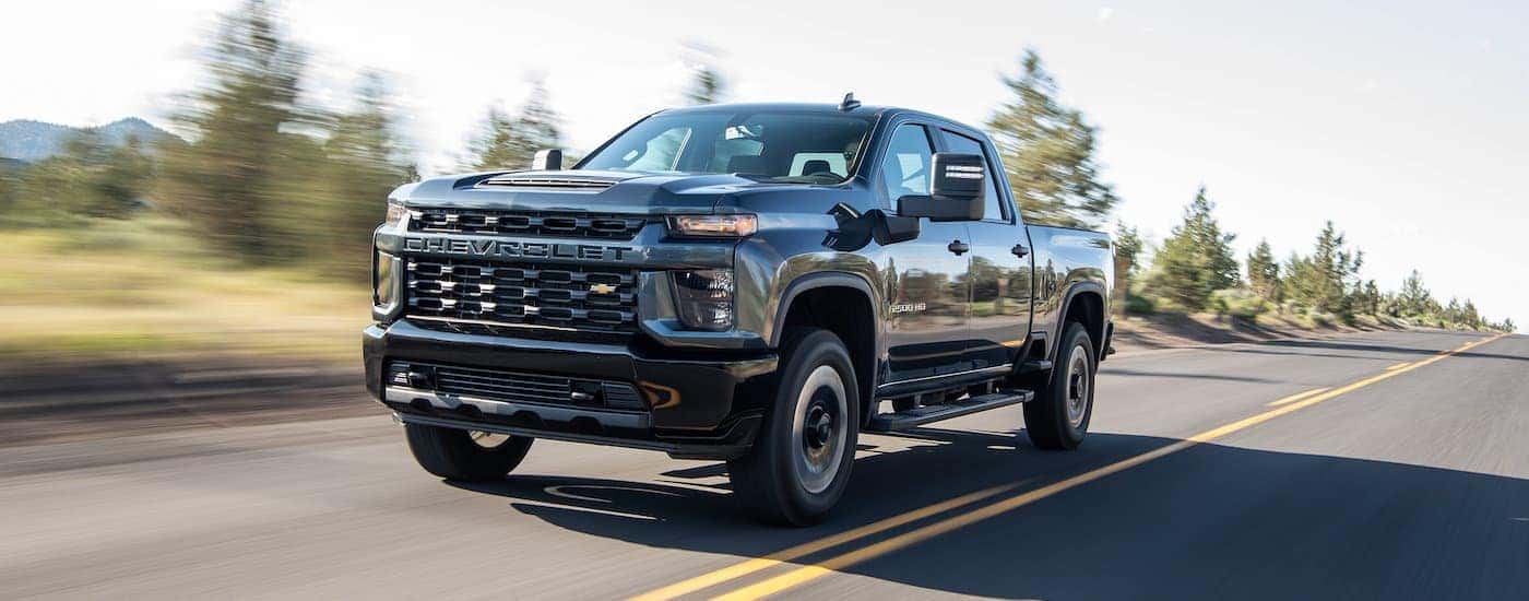A black 2020 Chevy certified pre-owned Silverado 1500HD is shown driving down a tree-lined road.