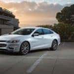A white 2015 Chevy Malibu is parked in a driveway at dusk.
