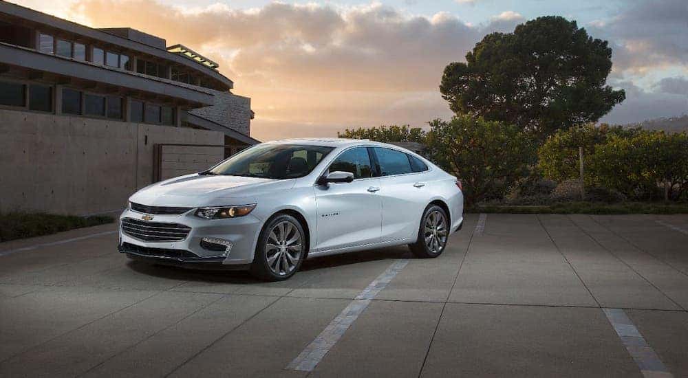 A white 2015 Chevy Malibu is parked in a driveway at dusk.
