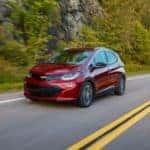 A maroon 2017 Chevy Bolt EV is shown driving down an empty road after leaving an Albany electric car dealer.