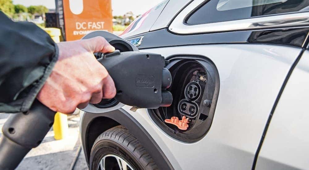 A close up shows a person plugging a charge cable into a grey 2018 Chevy Bolt EV.