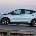 A 2022 light blue Chevy Bolt EV is driving on a wooden ramp near the beach after leaving a Chevy EV dealer.