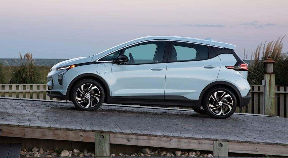 A 2022 light blue Chevy Bolt EV is driving on a wooden ramp near the beach after leaving a Chevy EV dealer.