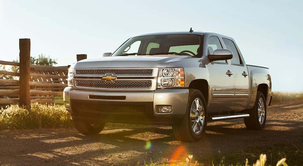 A silver 2013 Chevy Silverado is parked next to a fence.