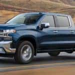 A blue 2021 Chevy Silverado is driving down a two way road past a vineyard.