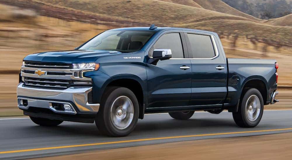 A blue 2021 Chevy Silverado is driving down a two way road past a vineyard.