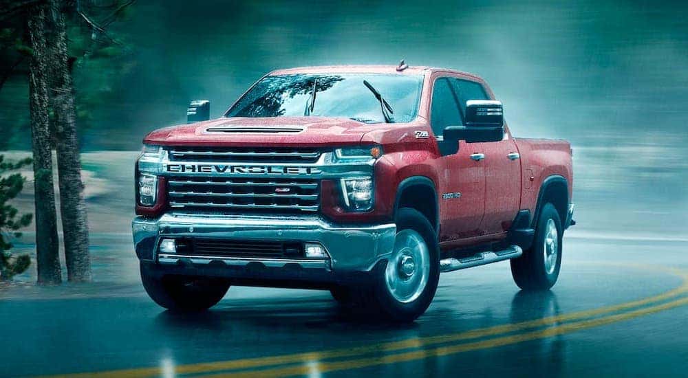 A red 2021 Chevy Silverado 2500 HD is shown rounding a corner in the rain after leaving a Chevrolet Silverado HD dealer.