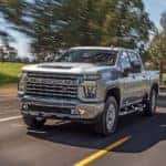 A silver 2021 Chevy Silverado 2500 HD Z71 is shown driving down a tree lined road.