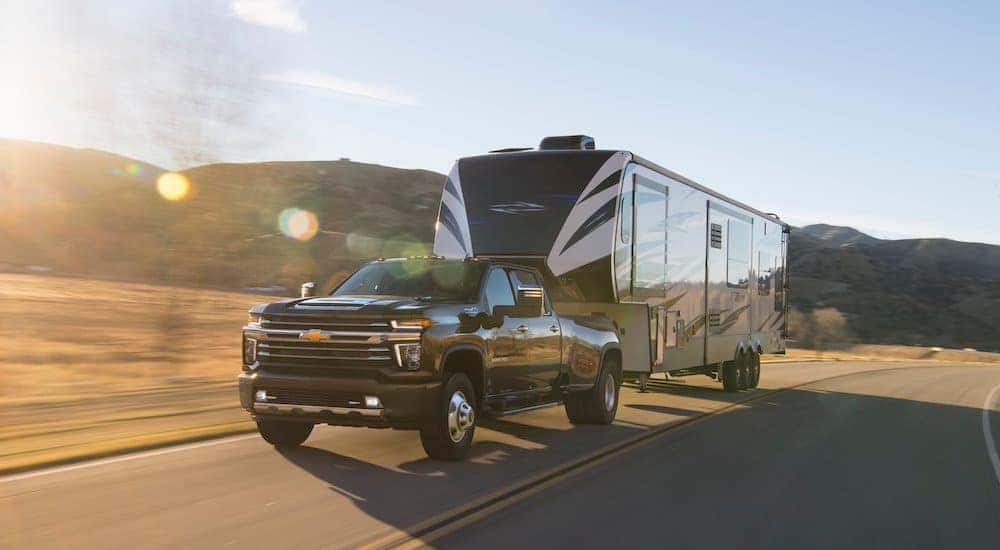 A black 2021 Chevy Silverado 3500 HD is shown towing a trailer down a sunny road.