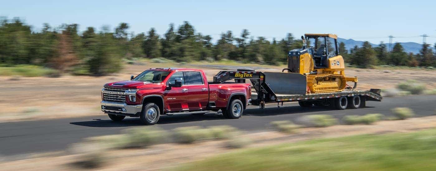 A red 2021 Chevy Silverado 3500 HD is shown towing construction equipment.