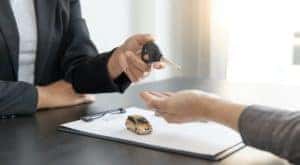 A salesman is passing a set of keys to a car buyer after signing paperwork.