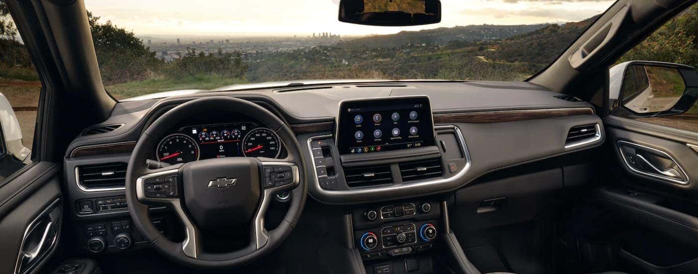 The black interior of a 2021 Chevy Tahoe shows the steering wheel and infotainment screen.