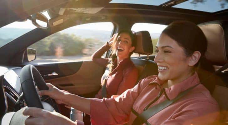 Two women are driving in a Chevy vehicle with the sun shining.