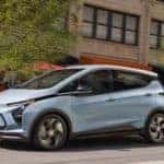 A light blue 2022 Chevy Bolt EV is shown driving through a city after look at new Chevy Vehicles in stock.