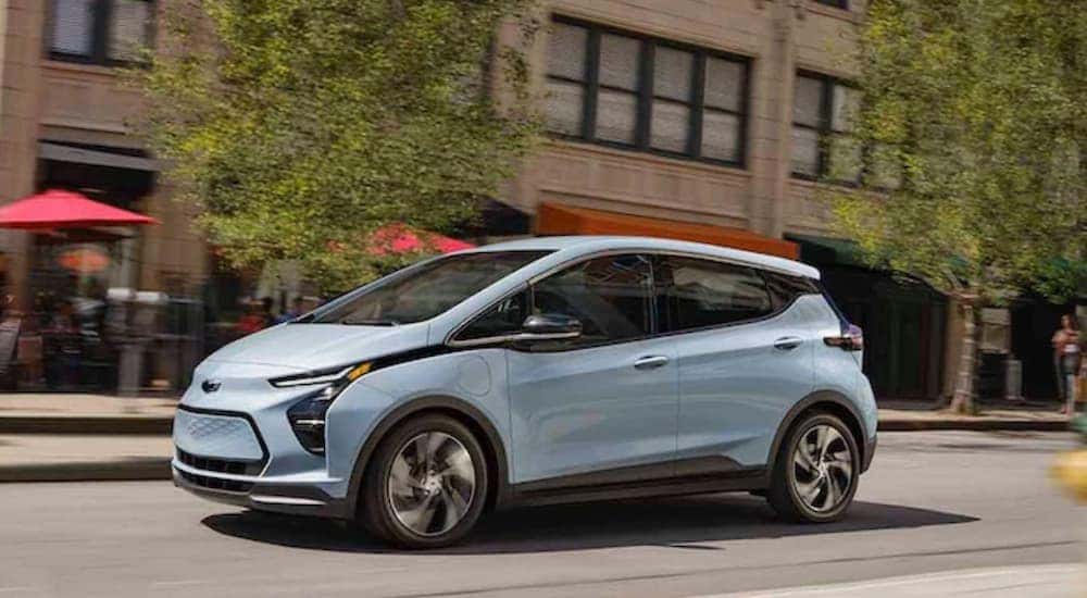 A light blue 2022 Chevy Bolt EV is shown driving through a city after look at new Chevy Vehicles in stock.