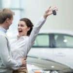 A couple is excited while a woman holds up a set of car keys.