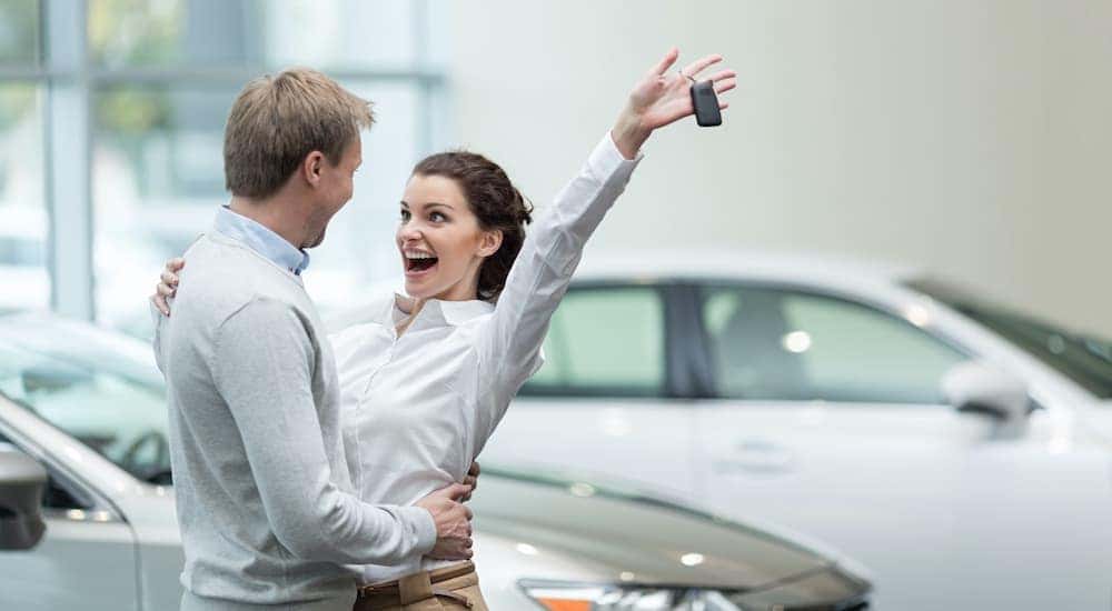 A couple is excited while a woman holds up a set of car keys.