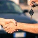 A salesman is shaking hands with a car buyer at an Albany used car dealership.